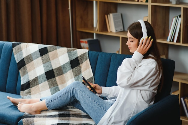 Beautiful young caucasian woman in casual clothing enjoying music and smiling while resting at home Young woman with headphones using laptop at home
