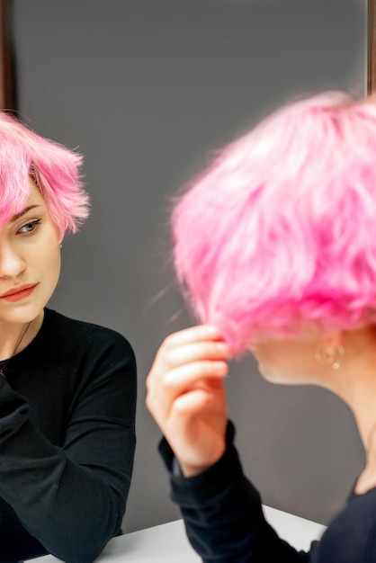 Bella giovane donna caucasica guardando i suoi corti capelli rosa in uno specchio.