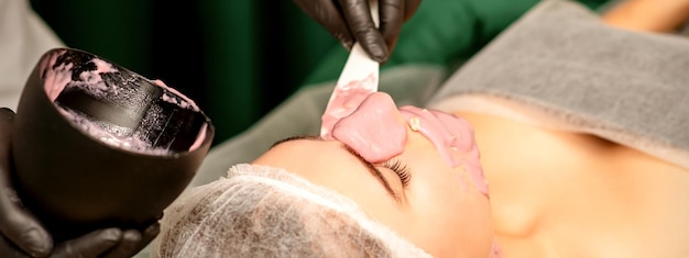 Beautiful young caucasian woman receiving an alginic mask to the face in beauty salon Facial skin treatment