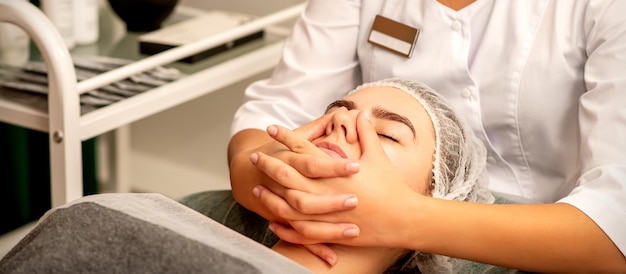 Foto bella giovane donna caucasica con gli occhi chiusi che riceve un massaggio facciale in un salone di bellezza