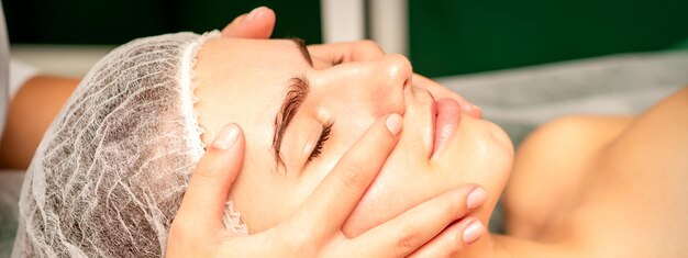 Beautiful young caucasian woman with closed eyes receiving a facial massage in a beauty salon