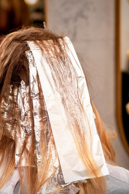 Beautiful young caucasian woman with foil in her hair while dyeing her hair sitting in a beauty salon