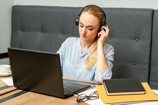 カフェのテーブルに座っているヘッドフォンとラップトップを持つ美しい若い白人女性