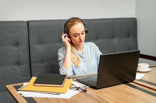 Beautiful young caucasian woman with headphones and laptop sitting at the table in a cafe