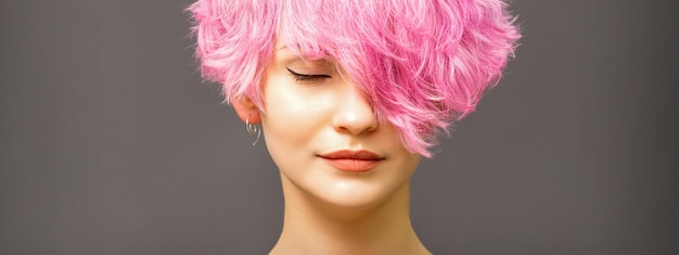 Beautiful young caucasian woman with short curly bob hairstyle dyed in pink color with closed eyes against dark gray background with copy space