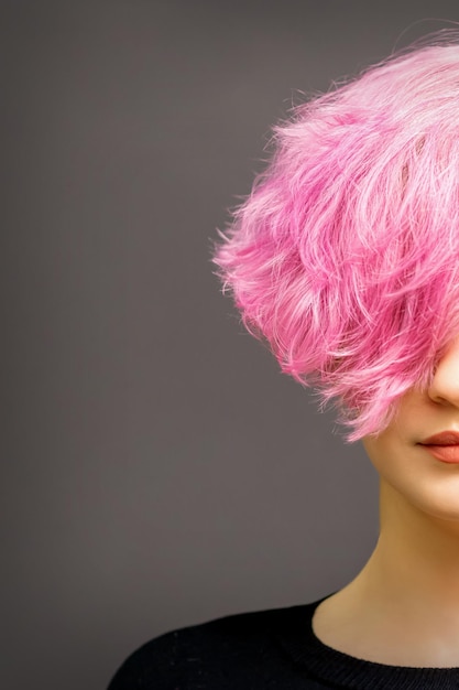 Beautiful young caucasian woman with short curly bob hairstyle dyed in pink color with closed eyes against dark gray background with copy space