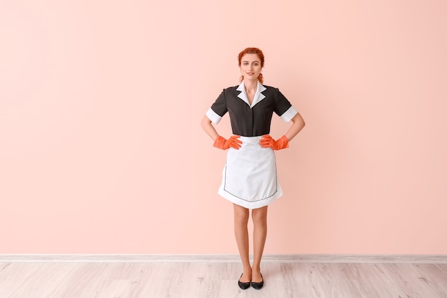 Beautiful young chambermaid near color wall