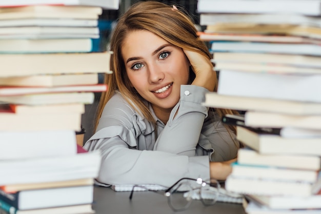 Beautiful young college student woman in a library, posing with glasses and books