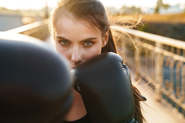 Beautiful young confident sportswoman with long brown hair boxing while standing at the bridge