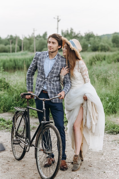 Beautiful young couple bride and groom walking in a field with a bicycle