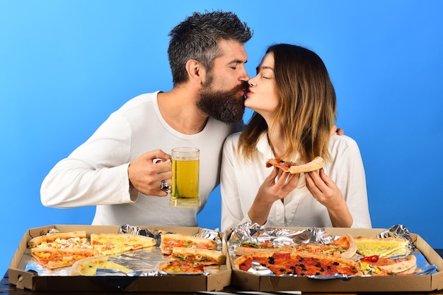 ピザを食べてビールを飲み、愛の食べ物と飲み物にキスをする美しい若いカップル幸せな家族