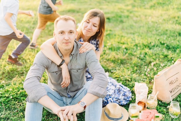 Beautiful young couple enjoying picnic time on the sunset they sitting in a meadow on the grass and