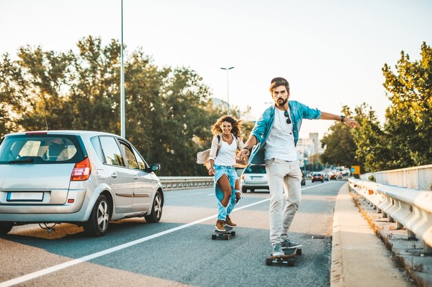 Beautiful young couple enjoying skateboarding on city street