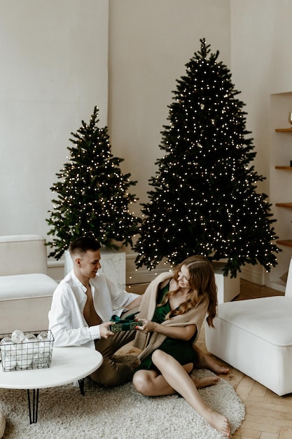 Beautiful young couple exchanging Christmas gifts at home in a bright living room