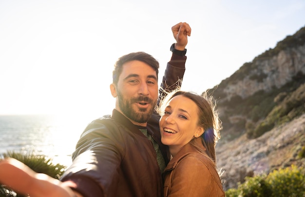 Beautiful young couple having fun taking a selfie portrait against a beautiful panorama at sunset Boyfriend and girlfriend in love smiling at the camera together People and lifestyle concept