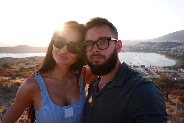 Beautiful young couple of hipsters in fashionable clothes on the background of the sea Bearded guy tshirt wearing sunglasses smiling happy lovers on the beach by the sea