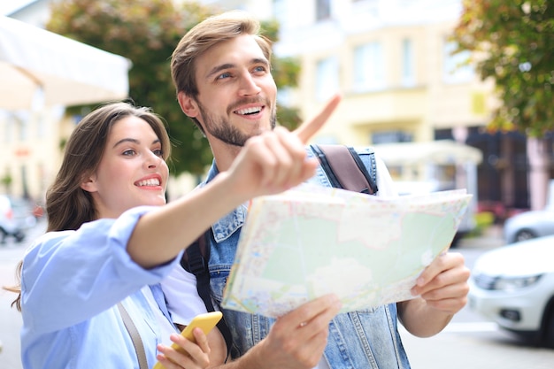 Foto bella giovane coppia che tiene una mappa e sorride mentre sta in piedi all'aperto.