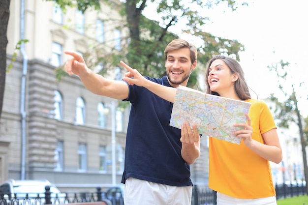 Beautiful young couple holding a map and smiling while standing outdoors.