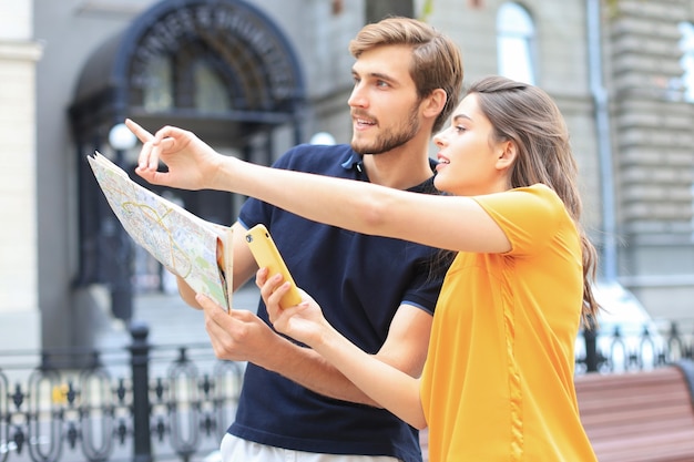 Photo beautiful young couple holding a map and smiling while standing outdoors.