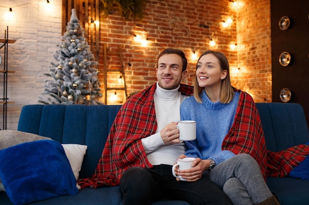 Beautiful young couple at home drinking coffee at Christmas morning. Spending time together, relationships and people concept. Winter holidays, Christmas celebrations, New Year concept.