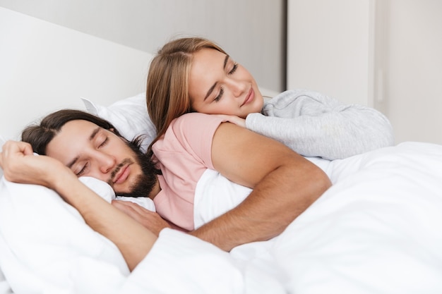 Beautiful young couple laying in bed at home, embracing while sleeping