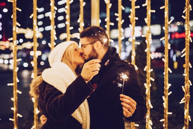 Beautiful young couple in love enjoying Christmas or New Year night on a city street.