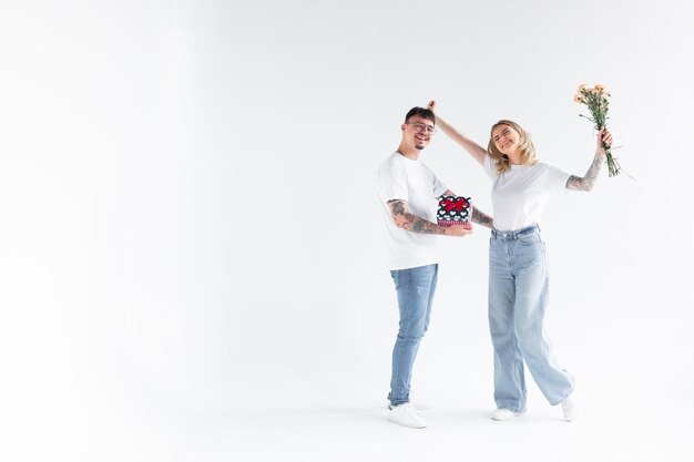 Beautiful young couple in love at home celebrating with a gift box and flowers