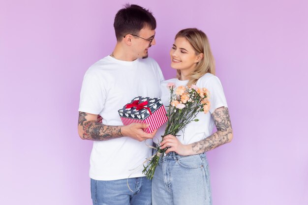 Beautiful young couple in love at home celebrating with a gift box and flowers