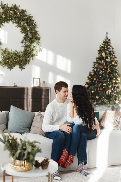 Beautiful young couple in love in socks with Christmas pattern looking to each other at living room decorated for Christmas.