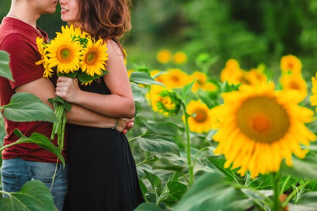 A beautiful young couple a man and a woman embrace in a field of sunflowers at sunset