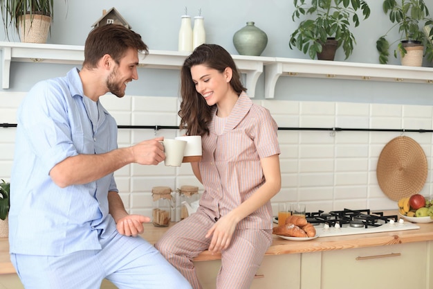 Beautiful young couple in pajamas is looking at each other and smiling while cooking in kitchen at home.