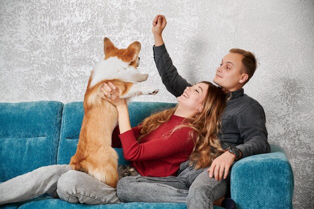 Beautiful young couple playing with cute Corgi at home