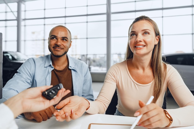 Beautiful young couple signs documents at car dealership showroom