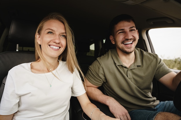 Beautiful young couple sitting on front passenger seats and driving a car