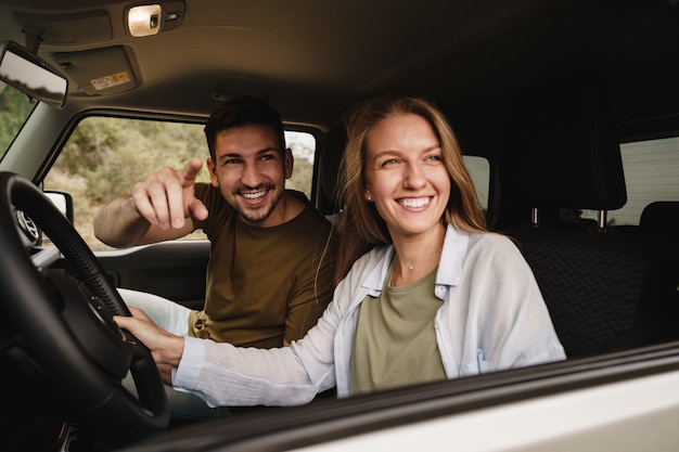 Beautiful young couple sitting on front passenger seats and driving a car