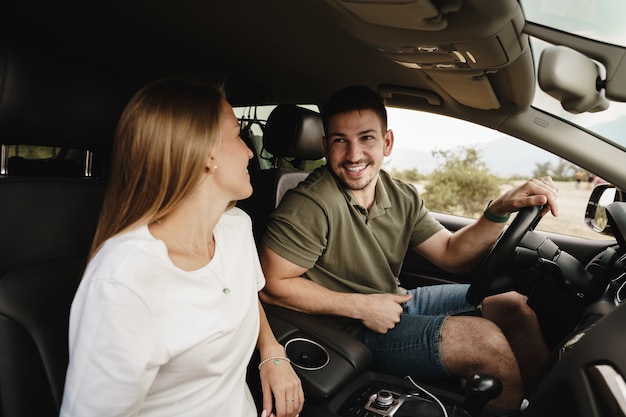 Beautiful young couple sitting on front passenger seats and driving a car