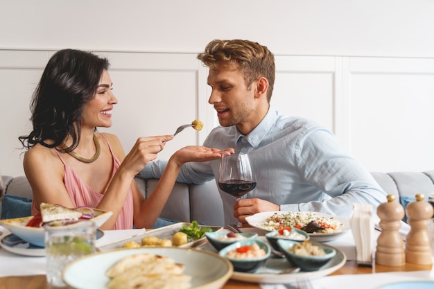 Beautiful young couple sitting at the table with delicious food and wine in restaurant
