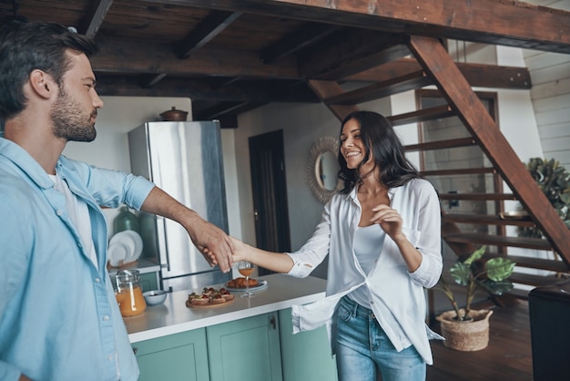 Beautiful young couple smiling and dancing while spending time in the kitchen