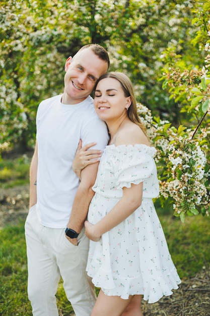 Beautiful young couple in spring garden Beauty lifestyle family concept A happy mother is expecting a baby A happy young couple in a blooming garden