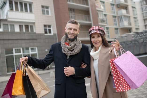 beautiful young couple standing with shopping bags while showing their purchases to you