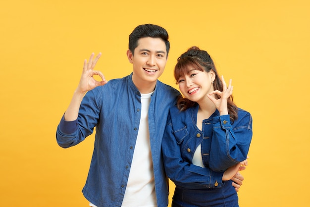 Beautiful young couple together standing over isolated yellow background looking surprised and shocked doing ok approval symbol with fingers. Crazy expression