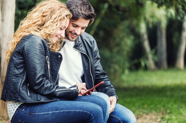 Beautiful young couple using they mobile phone in the park.