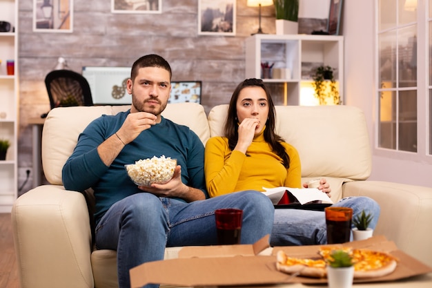 Bella giovane coppia che guarda la tv e mangia fast food da asporto in soggiorno