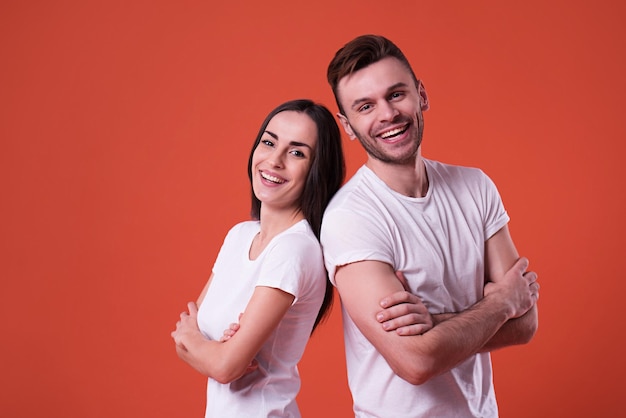 Beautiful young couple in white blank t-shirts are posing on orange background. Relationship, family, advertising