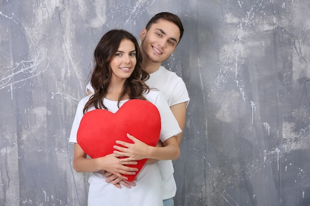 Beautiful young couple with pillow in heart shape on grunge wall 