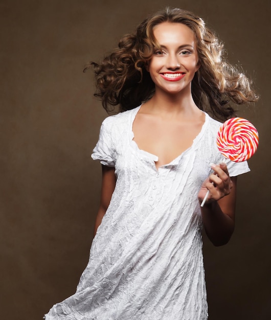 Beautiful young curly girl holding a red white lollipop and smiling