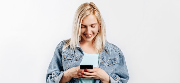 Beautiful young cute girl smiling and looking at phone on gray isolated background