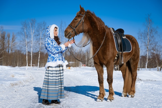 Beautiful young darkhaired woman in traditional clothes riding a horse in winter