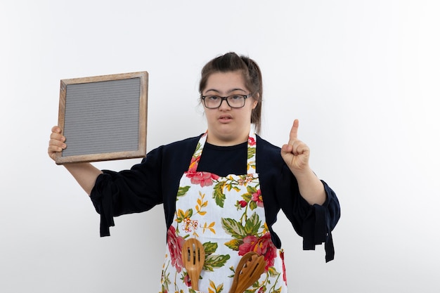 Beautiful young down syndrome girl in colorful apron holding empty frame.