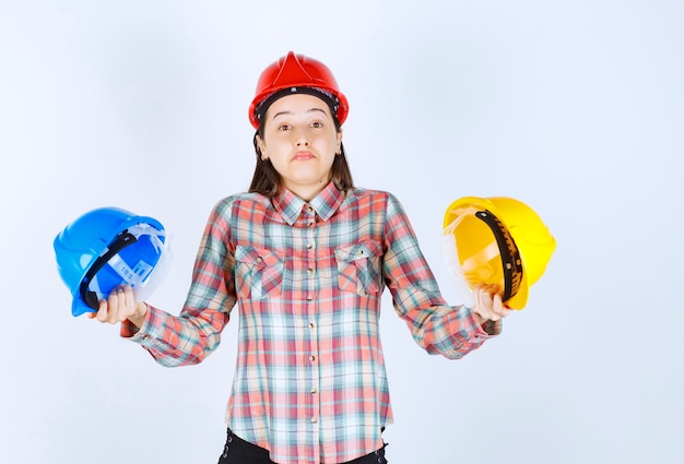 Beautiful young engineer holding security helmets and standing on white background. 